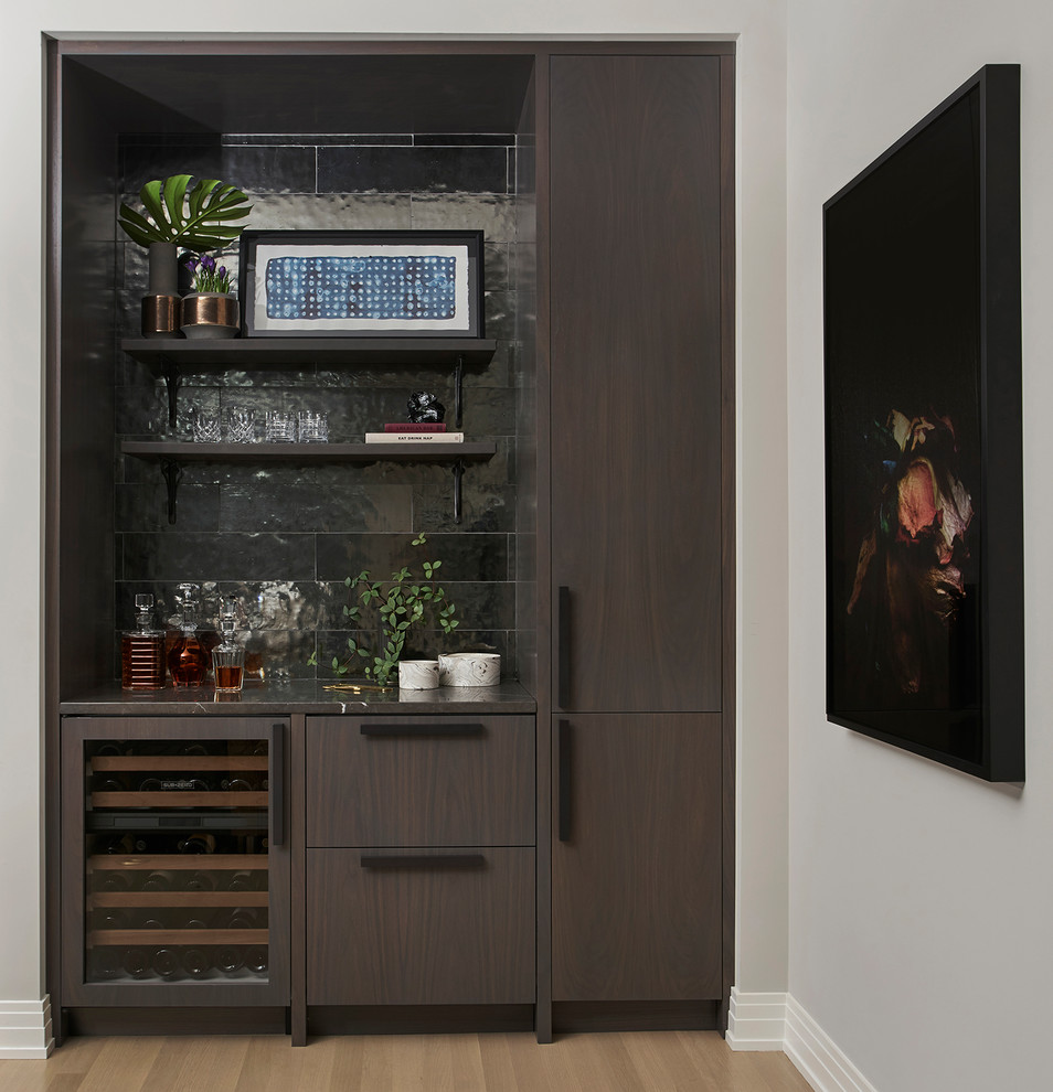 This is an example of a contemporary single-wall home bar in Chicago with flat-panel cabinets, dark wood cabinets, black splashback, medium hardwood floors and beige floor.