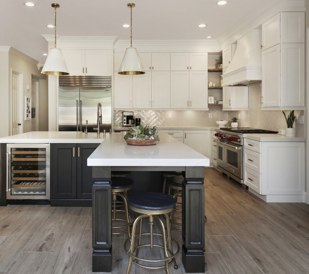 Design ideas for a transitional open plan kitchen in Los Angeles with a farmhouse sink, shaker cabinets, beige splashback, stainless steel appliances, medium hardwood floors, with island, brown floor and white benchtop.
