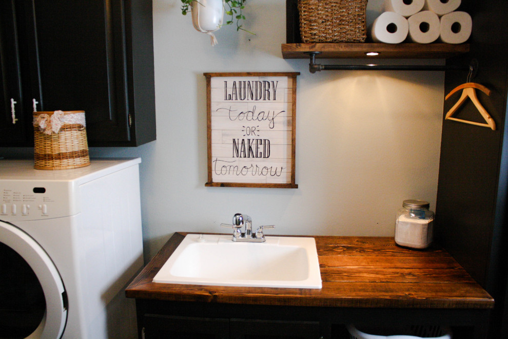 Design ideas for a mid-sized industrial single-wall dedicated laundry room in Other with an utility sink, shaker cabinets, black cabinets, wood benchtops, blue walls, linoleum floors, a side-by-side washer and dryer, beige floor and brown benchtop.