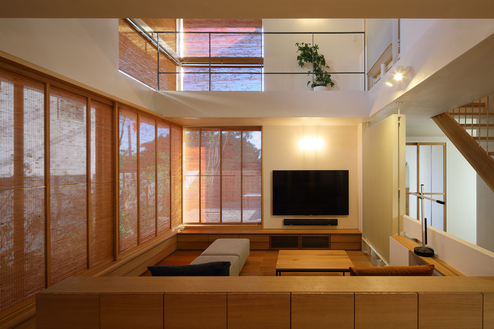 Photo of an asian living room in Kobe with white walls, medium hardwood floors, a wall-mounted tv and brown floor.