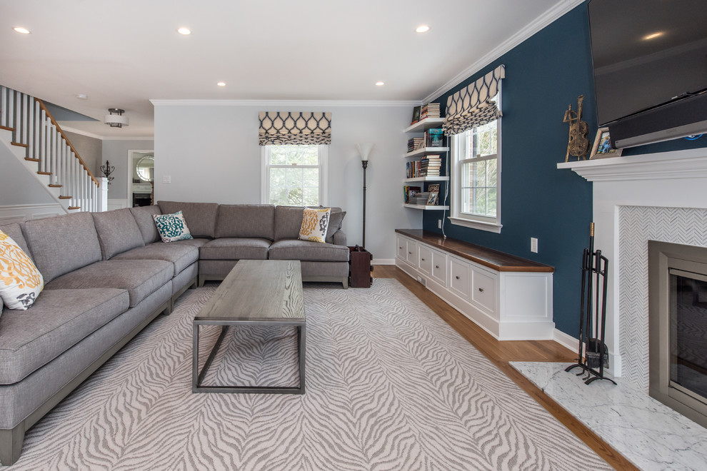 Mid-sized traditional open concept family room in DC Metro with a library, blue walls, light hardwood floors, a standard fireplace, a wood fireplace surround, a wall-mounted tv and brown floor.