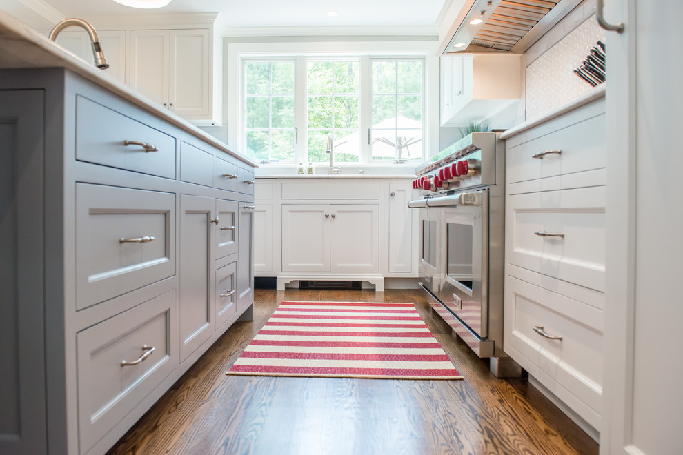 Large transitional l-shaped eat-in kitchen in Portland Maine with an undermount sink, shaker cabinets, white cabinets, white splashback, stainless steel appliances, light hardwood floors, with island, marble benchtops and subway tile splashback.