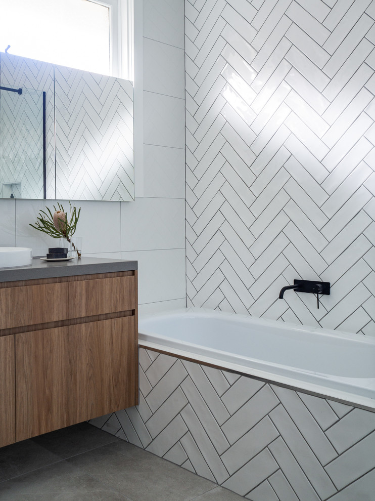 Inspiration for a bathroom in Melbourne with flat-panel cabinets, light wood cabinets, a drop-in tub, a corner shower, white tile, porcelain tile, white walls, porcelain floors, a trough sink, engineered quartz benchtops, grey floor, a hinged shower door and grey benchtops.