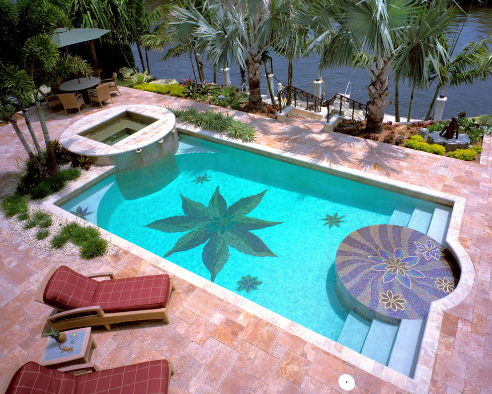 This is an example of a mid-sized tropical backyard rectangular infinity pool in Miami with natural stone pavers and a hot tub.