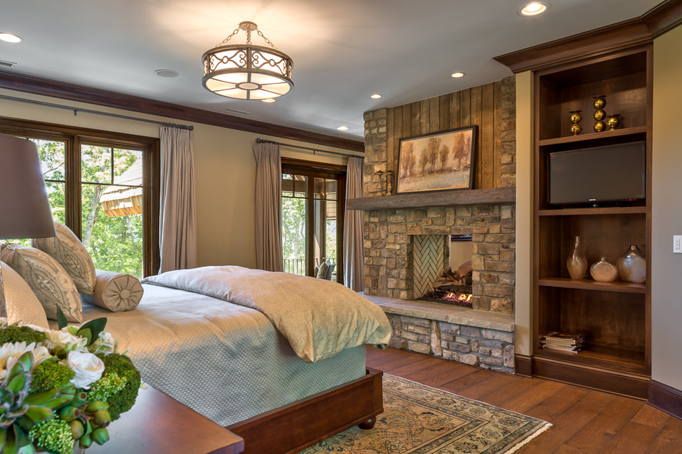 This is an example of a mid-sized country loft-style bedroom in Other with black walls, medium hardwood floors, a two-sided fireplace, a stone fireplace surround and brown floor.