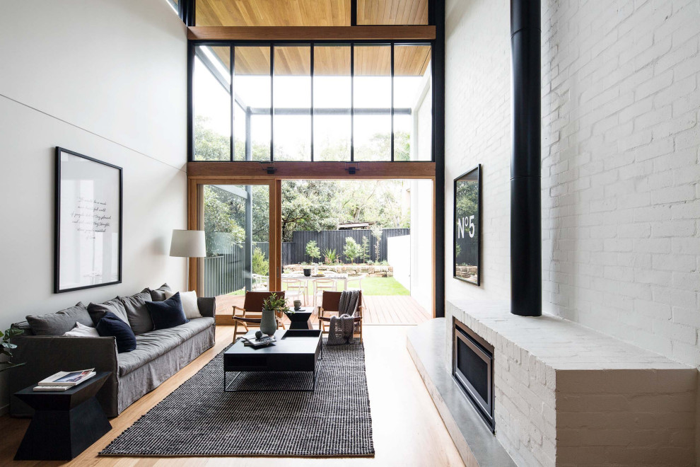 Design ideas for a mid-sized contemporary loft-style living room in Sydney with white walls, medium hardwood floors, a standard fireplace, a brick fireplace surround and timber.