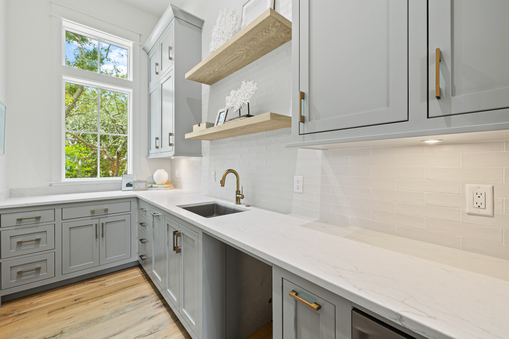Design ideas for a mid-sized beach style l-shaped kitchen pantry in Miami with an undermount sink, shaker cabinets, blue cabinets, quartz benchtops, white splashback, terra-cotta splashback, stainless steel appliances, light hardwood floors and white benchtop.