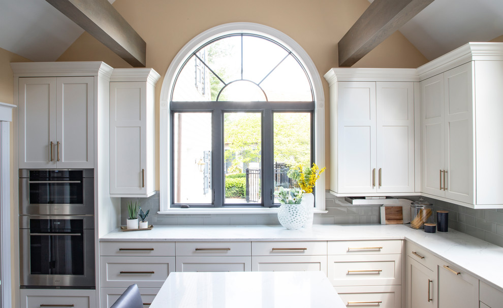 Kitchen - large transitional u-shaped medium tone wood floor kitchen idea with an undermount sink, white cabinets, quartz countertops, gray backsplash, glass tile backsplash, stainless steel appliances, an island and white countertops
