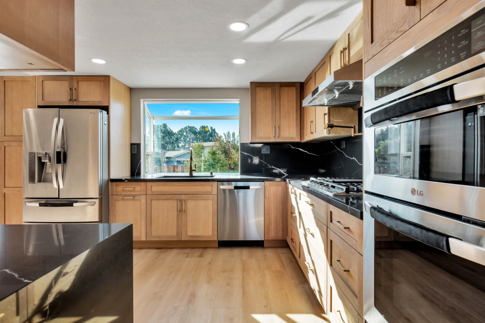 This is an example of a mid-sized midcentury l-shaped separate kitchen in Phoenix with an undermount sink, shaker cabinets, brown cabinets, quartz benchtops, black splashback, engineered quartz splashback, stainless steel appliances, vinyl floors, no island, brown floor and black benchtop.