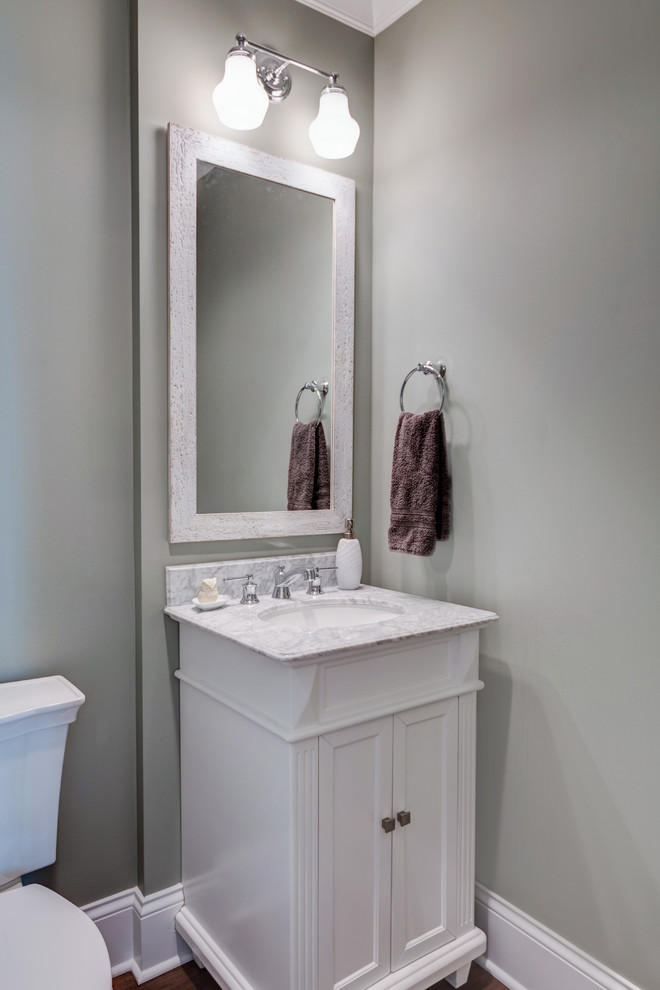 Inspiration for a mid-sized arts and crafts powder room in Indianapolis with recessed-panel cabinets, white cabinets, a two-piece toilet, grey walls, dark hardwood floors, an undermount sink, marble benchtops, brown floor and grey benchtops.