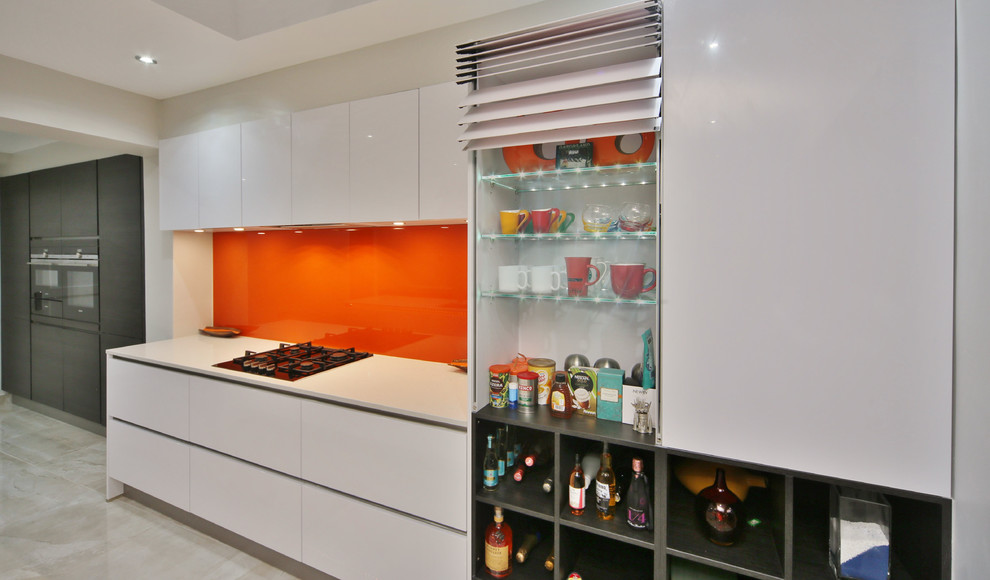 Inspiration for a mid-sized contemporary single-wall open plan kitchen in London with an undermount sink, flat-panel cabinets, white cabinets, quartzite benchtops, orange splashback, glass sheet splashback, black appliances, porcelain floors, with island, beige floor and white benchtop.