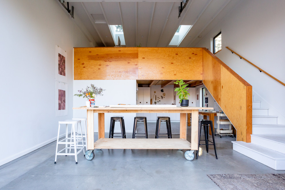 Immagine di un atelier industriale di medie dimensioni con pareti bianche, pavimento in cemento, scrivania autoportante, pavimento grigio e travi a vista