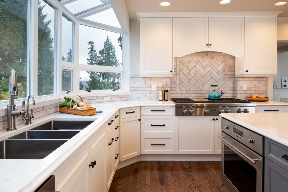 Design ideas for a large traditional u-shaped eat-in kitchen in Seattle with a triple-bowl sink, shaker cabinets, grey cabinets, quartz benchtops, beige splashback, ceramic splashback, stainless steel appliances, dark hardwood floors, with island, brown floor and white benchtop.