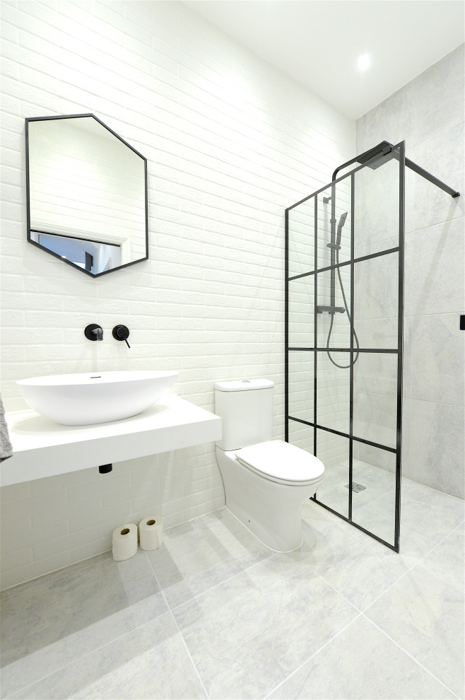 Inredning av ett industriellt litet vit vitt badrum med dusch, med släta luckor, vita skåp, en öppen dusch, en toalettstol med hel cisternkåpa, vit kakel, tunnelbanekakel, vita väggar, ett väggmonterat handfat, bänkskiva i kvarts, vitt golv och med dusch som är öppen