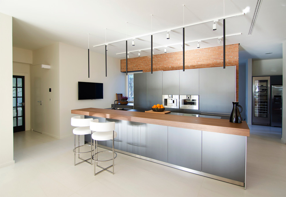 Modelo de cocina lineal contemporánea grande abierta con armarios con paneles lisos, puertas de armario grises, electrodomésticos de acero inoxidable, una isla y fregadero integrado