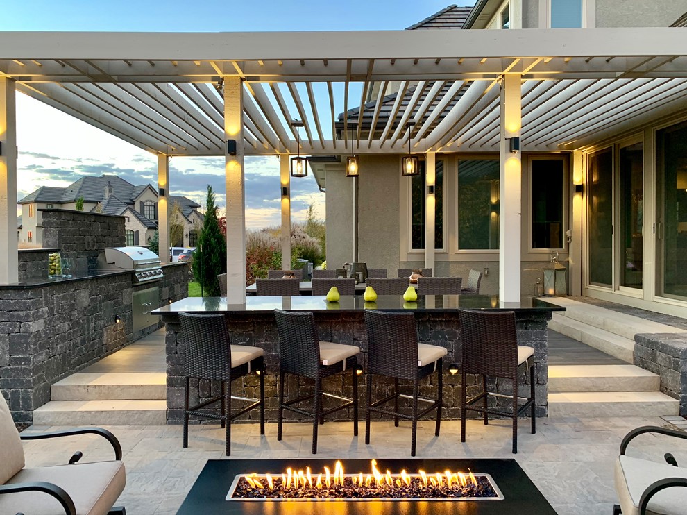 This is an example of a modern backyard patio in Kansas City with a fire feature, concrete pavers and a pergola.