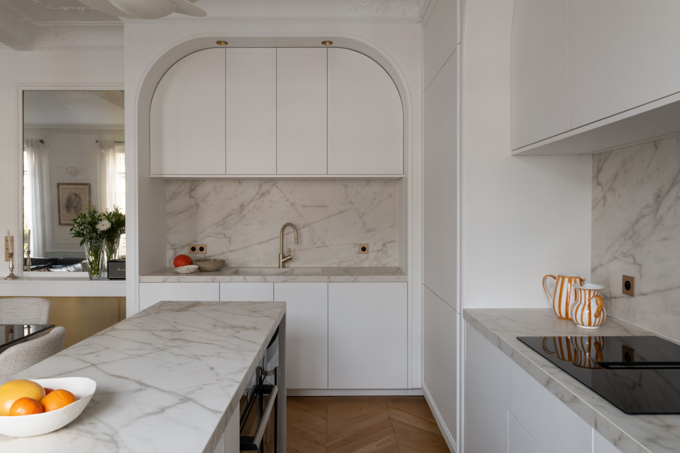 Aménagement de cuisine ouverte in L With un évier encastré, des portes de placard blanches, plan de travail en marbre, une crédence blanche, une crédence en marbre, un électroménager blanc, îlot, un plan de travail blanc, un placard à porte plane, un sol en bois brun and un sol marron.