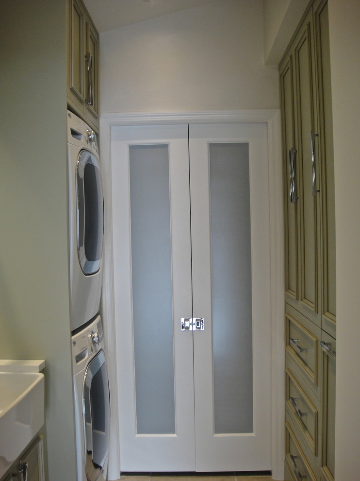 Inspiration for a transitional galley dedicated laundry room in Miami with a farmhouse sink, recessed-panel cabinets, green cabinets, quartz benchtops, beige walls, ceramic floors and a stacked washer and dryer.