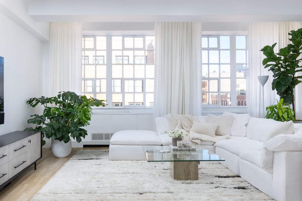 Large contemporary loft-style family room in New York with white walls, light hardwood floors and a wall-mounted tv.