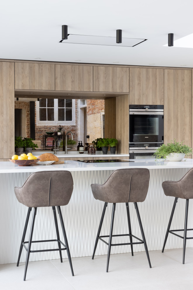 Inspiration for a mid-sized scandinavian eat-in kitchen in Hampshire with flat-panel cabinets, medium wood cabinets, solid surface benchtops, mirror splashback, black appliances, with island and white benchtop.