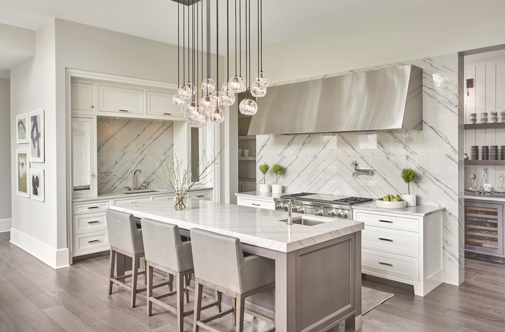Photo of a transitional kitchen in Chicago with an undermount sink, shaker cabinets, white cabinets, white splashback, stainless steel appliances, light hardwood floors, with island and beige floor.