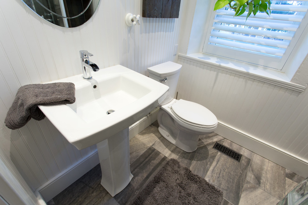 Inspiration for a mid-sized beach style bathroom in Toronto with gray tile, porcelain tile, multi-coloured walls, porcelain floors, a pedestal sink, glass benchtops, a corner shower and a two-piece toilet.