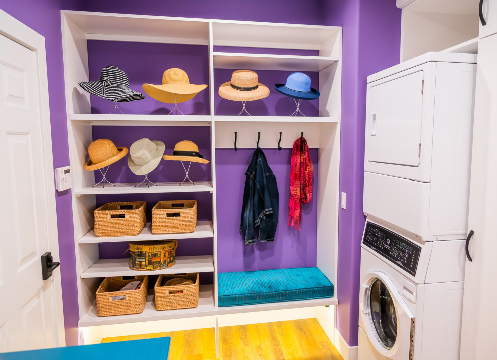 Photo of a modern utility room in Cedar Rapids with purple walls, medium hardwood floors, a stacked washer and dryer and brown floor.