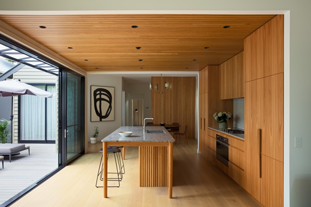 Example of a large trendy medium tone wood floor and wood ceiling eat-in kitchen design in Melbourne with an undermount sink, flat-panel cabinets, light wood cabinets, granite countertops, beige backsplash, mosaic tile backsplash, stainless steel appliances, an island and multicolored countertops