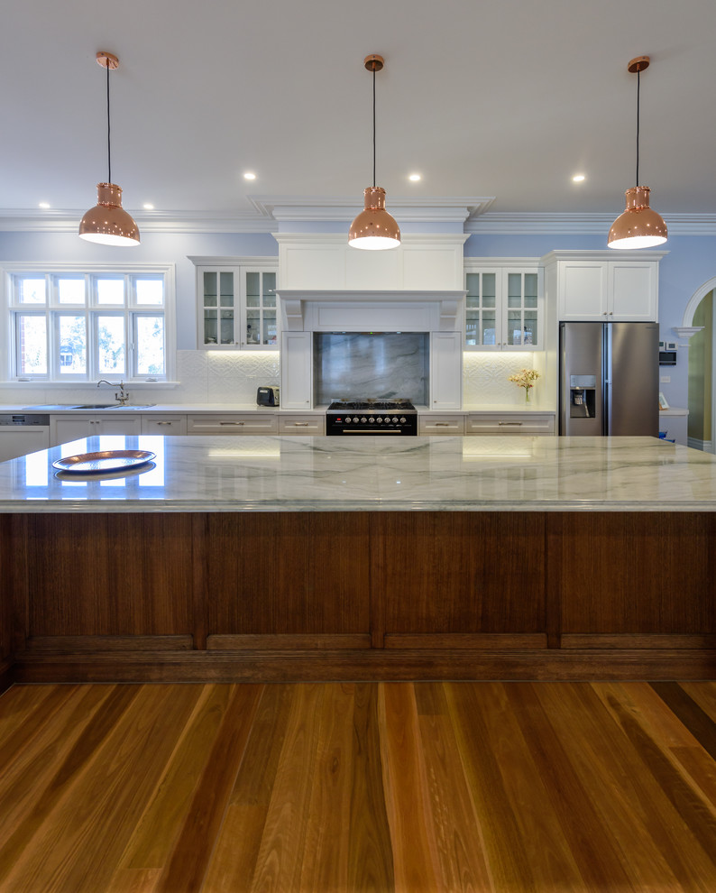 Inspiration for an expansive traditional l-shaped open plan kitchen in Melbourne with a double-bowl sink, recessed-panel cabinets, dark wood cabinets, quartzite benchtops, white splashback, ceramic splashback, black appliances, medium hardwood floors and with island.