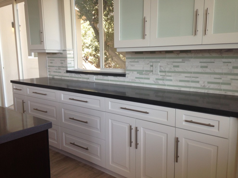 Inspiration for a mid-sized transitional l-shaped travertine floor eat-in kitchen remodel in Los Angeles with white cabinets, solid surface countertops, multicolored backsplash, stainless steel appliances, an island, marble backsplash and recessed-panel cabinets