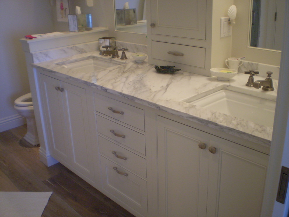 Photo of a mid-sized tropical master bathroom in Miami with an undermount sink, beaded inset cabinets, white cabinets, marble benchtops, a one-piece toilet, white tile, subway tile, white walls and light hardwood floors.