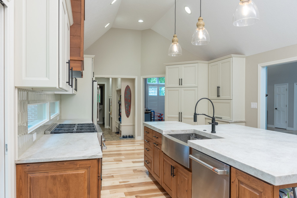 This is an example of a large transitional galley eat-in kitchen in Indianapolis with a farmhouse sink, raised-panel cabinets, medium wood cabinets, quartz benchtops, white splashback, glass tile splashback, stainless steel appliances, light hardwood floors, with island, brown floor, white benchtop and vaulted.