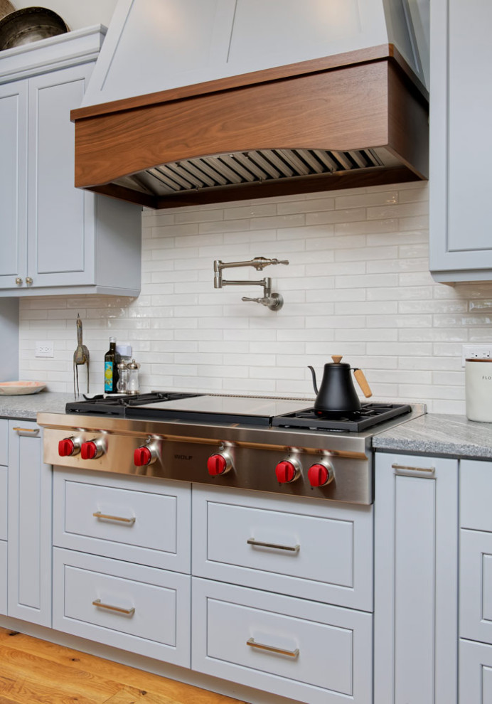Mid-sized mountain style l-shaped medium tone wood floor open concept kitchen photo with an undermount sink, shaker cabinets, granite countertops, beige backsplash, stainless steel appliances and an island