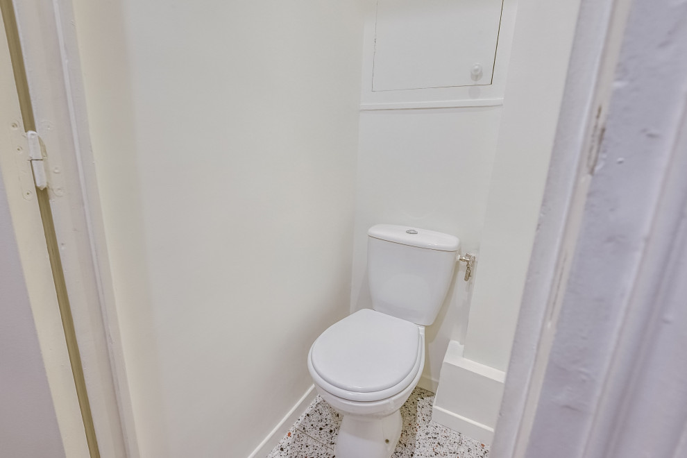 Réalisation d'un petit WC et toilettes design avec un placard à porte plane, des portes de placard blanches, WC à poser, un mur blanc, un sol en terrazzo, un sol multicolore et meuble-lavabo encastré.