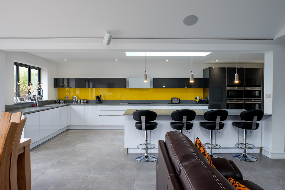 Inspiration for a large modern l-shaped open plan kitchen in Essex with a single-bowl sink, flat-panel cabinets, white cabinets, quartzite benchtops, yellow splashback, glass sheet splashback, black appliances, porcelain floors and with island.