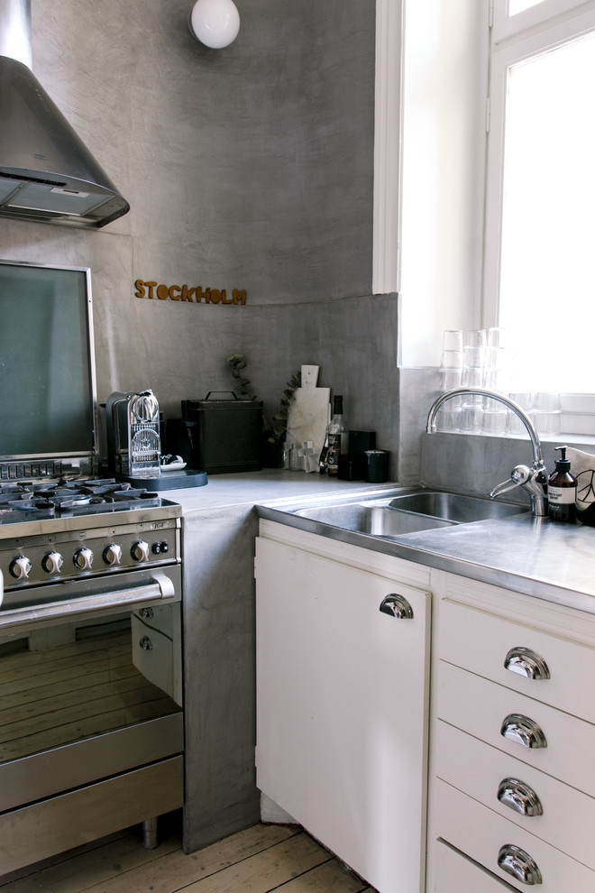 Design ideas for a small industrial l-shaped separate kitchen in Stockholm with a double-bowl sink, white cabinets, stainless steel benchtops, stainless steel appliances, light hardwood floors, raised-panel cabinets and no island.