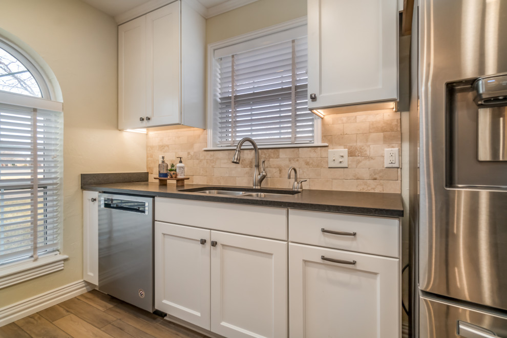 Eat-in kitchen - transitional galley vinyl floor and beige floor eat-in kitchen idea with a double-bowl sink, recessed-panel cabinets, white cabinets, granite countertops, beige backsplash, travertine backsplash, stainless steel appliances, a peninsula and black countertops
