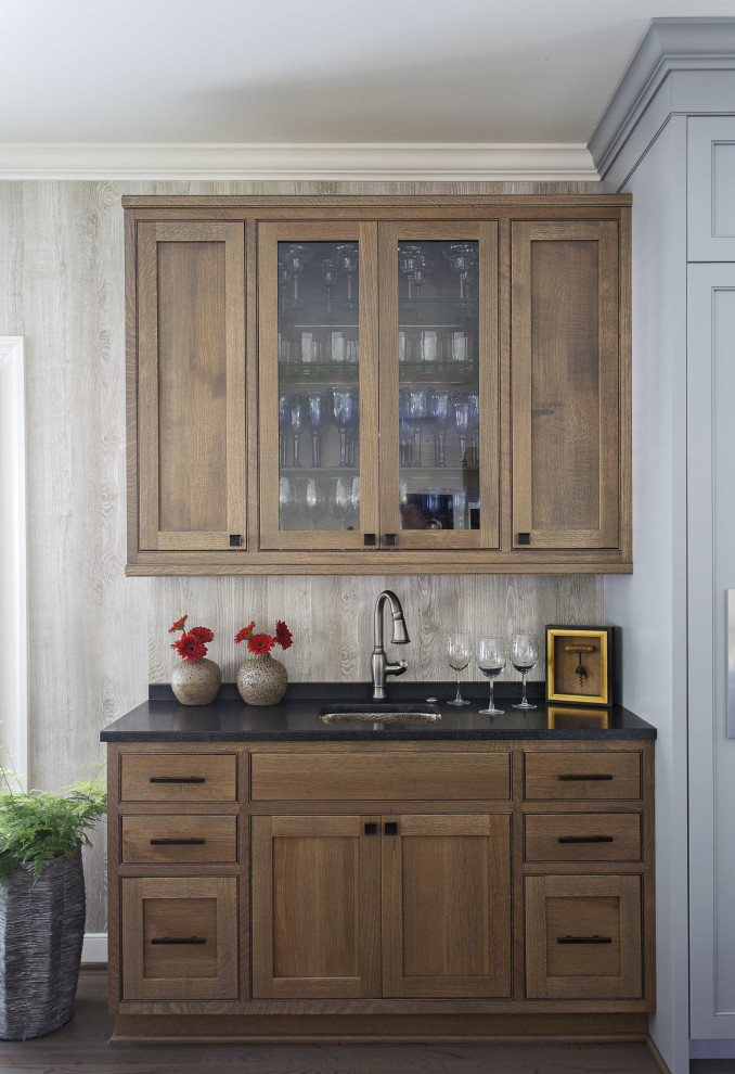 Inspiration for a beach style single-wall wet bar in Charleston with an undermount sink, glass-front cabinets, dark wood cabinets, dark hardwood floors and black benchtop.