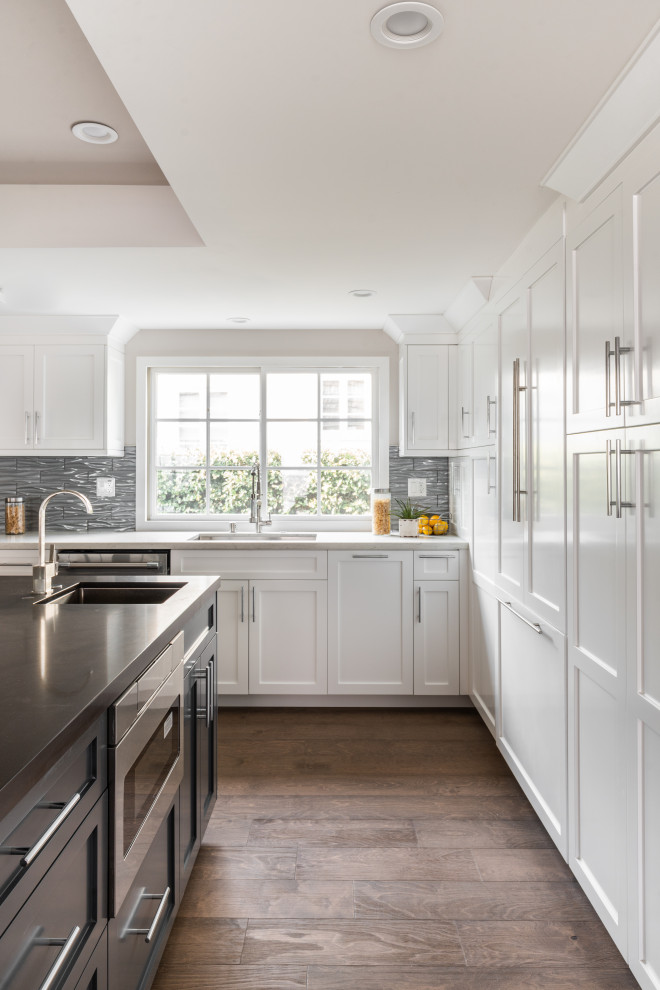 Photo of a large transitional l-shaped kitchen in Los Angeles with an undermount sink, shaker cabinets, white cabinets, grey splashback, panelled appliances, with island, brown floor and white benchtop.