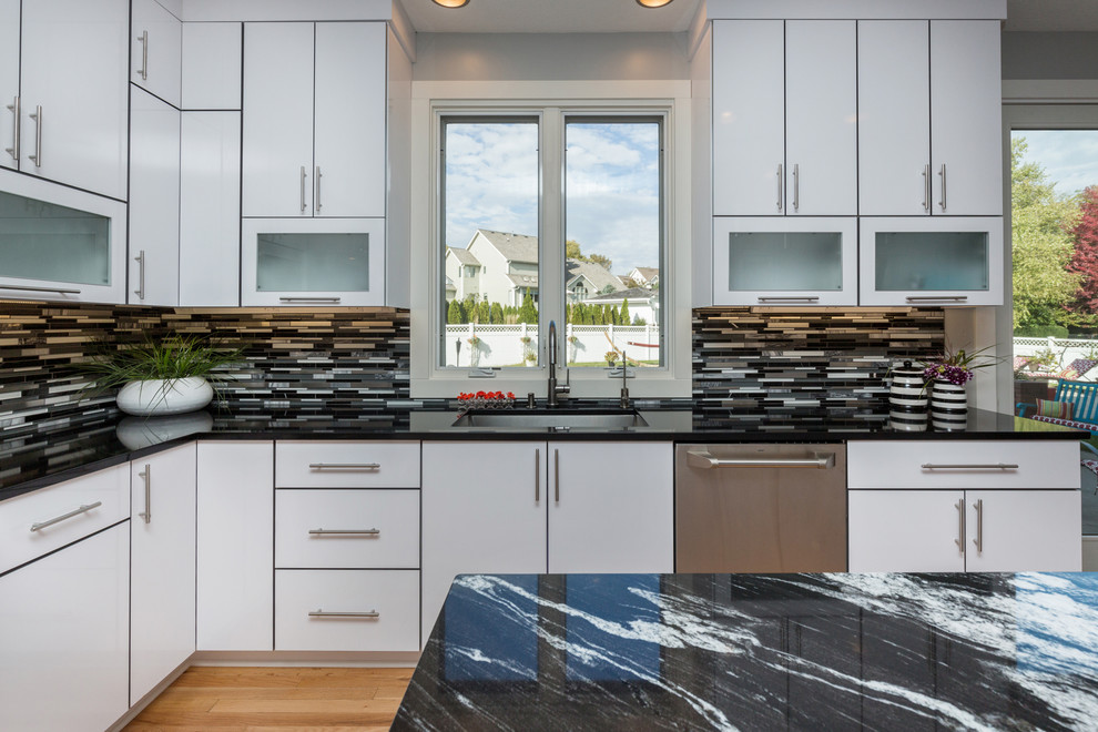 Open concept kitchen - large contemporary u-shaped light wood floor open concept kitchen idea with an undermount sink, flat-panel cabinets, white cabinets, granite countertops, multicolored backsplash, mosaic tile backsplash, stainless steel appliances and an island