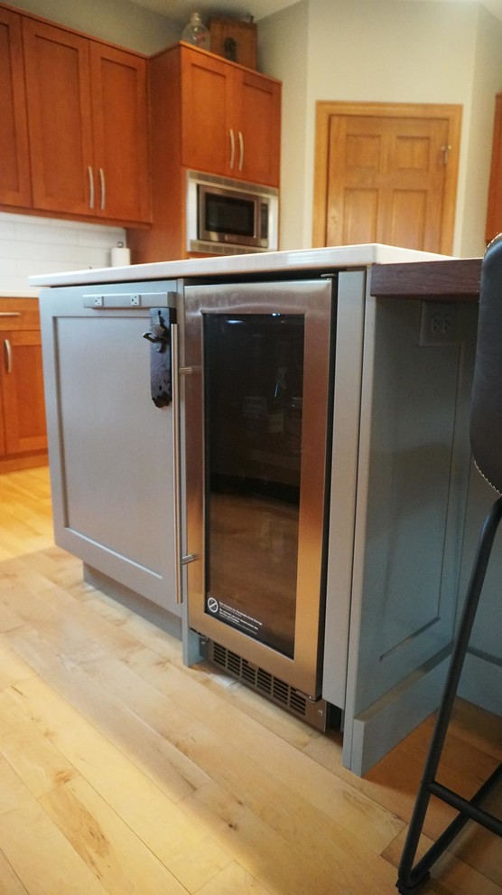 Large transitional l-shaped medium tone wood floor home design photo with an undermount sink, recessed-panel cabinets, brown cabinets, white backsplash, subway tile backsplash, stainless steel appliances, an island and white countertops