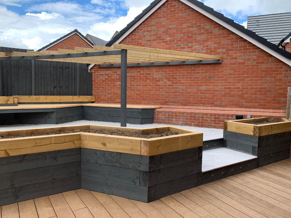 This is an example of a mid-sized contemporary sloped partial sun formal garden for spring in Buckinghamshire with with raised garden bed, decking and a wood fence.