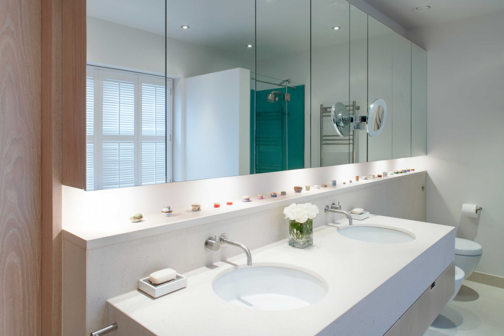 This is an example of a mid-sized contemporary kids bathroom in Sussex with a drop-in tub, green tile, mosaic tile, white walls, limestone floors, solid surface benchtops, a hinged shower door and white benchtops.