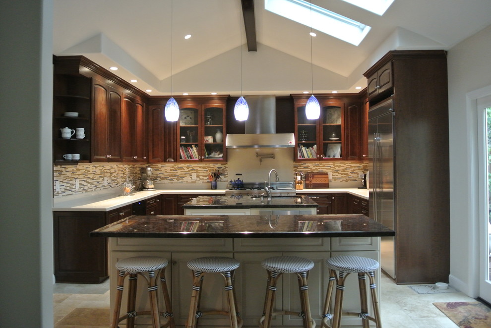 This is an example of a large transitional u-shaped eat-in kitchen in San Francisco with an undermount sink, raised-panel cabinets, dark wood cabinets, quartz benchtops, multi-coloured splashback, matchstick tile splashback, stainless steel appliances, travertine floors, multiple islands and beige floor.