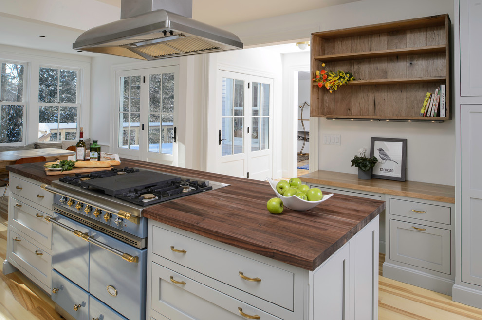 Mid-sized transitional l-shaped open plan kitchen in New York with a farmhouse sink, shaker cabinets, grey cabinets, wood benchtops, white splashback, subway tile splashback, stainless steel appliances, light hardwood floors and with island.