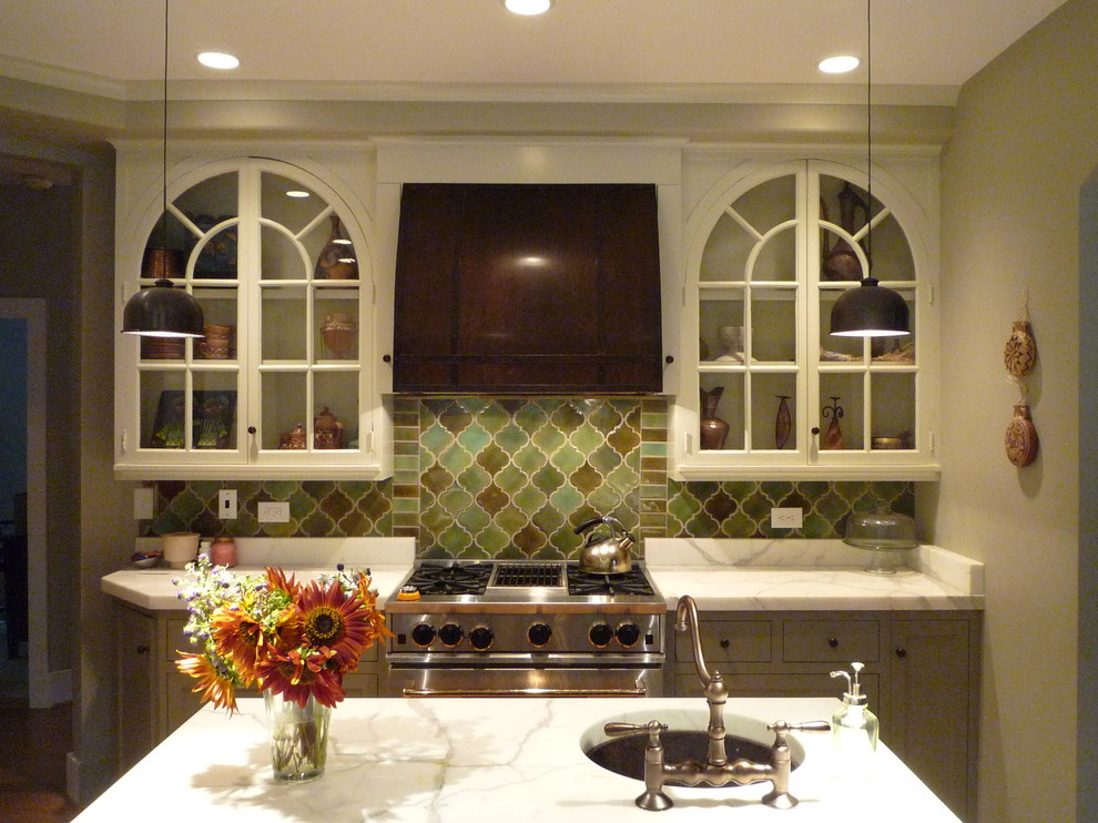 Example of a mid-sized transitional l-shaped medium tone wood floor and brown floor enclosed kitchen design with a farmhouse sink, shaker cabinets, marble countertops, ceramic backsplash, paneled appliances, white backsplash, an island and gray cabinets