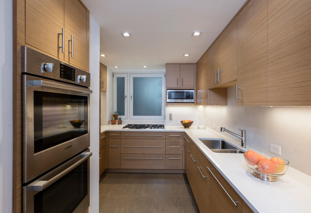 Inspiration for a mid-sized contemporary u-shaped kitchen in New York with an undermount sink, flat-panel cabinets, light wood cabinets, stainless steel appliances, no island, solid surface benchtops, beige splashback, stone slab splashback and light hardwood floors.