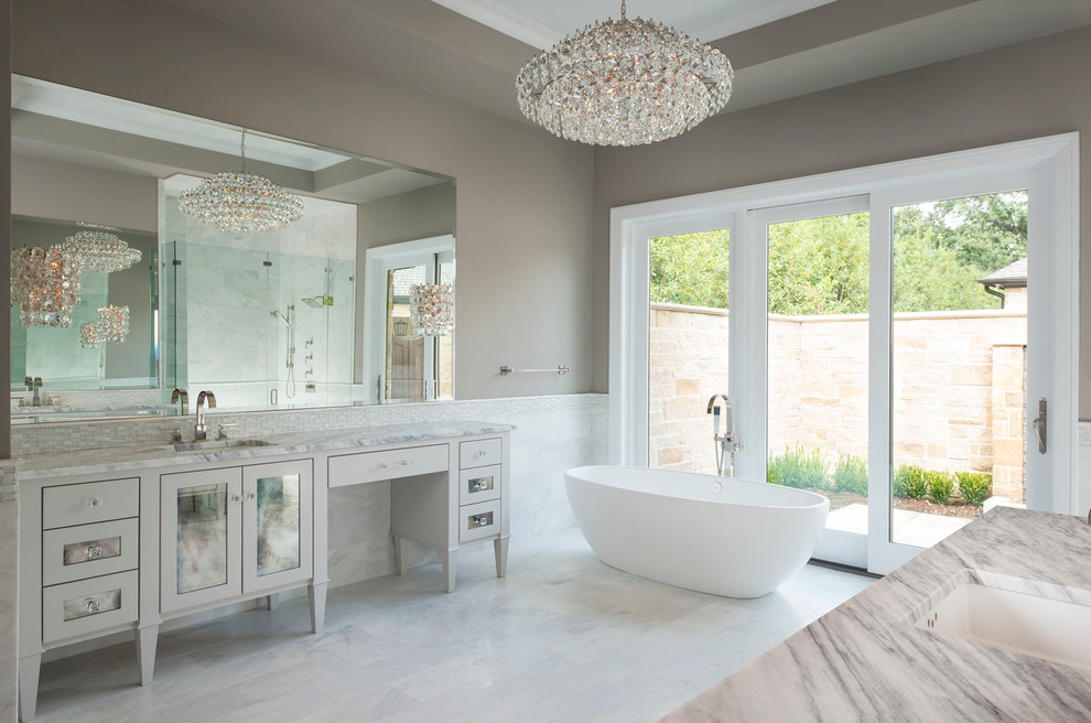 Photo of a large contemporary master bathroom in Dallas with grey cabinets, a freestanding tub, white tile, gray tile, grey walls, an undermount sink, an alcove shower, marble, marble floors, marble benchtops, white floor, a hinged shower door and glass-front cabinets.