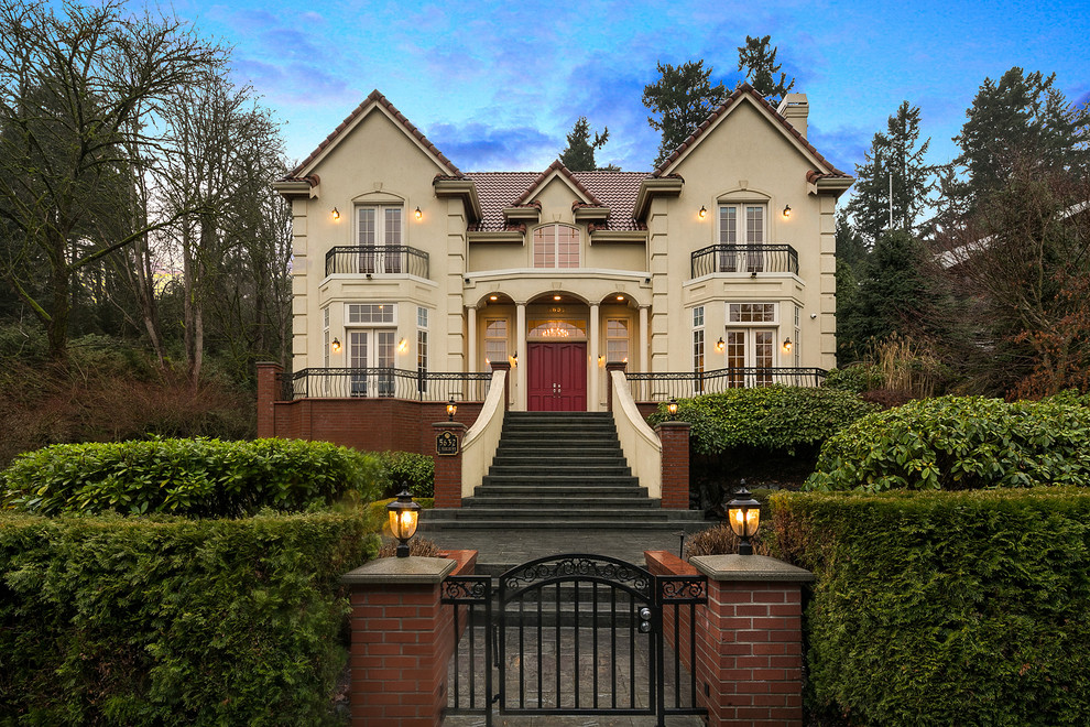 This is an example of a traditional two-storey stucco beige house exterior in Seattle with a gable roof and a tile roof.