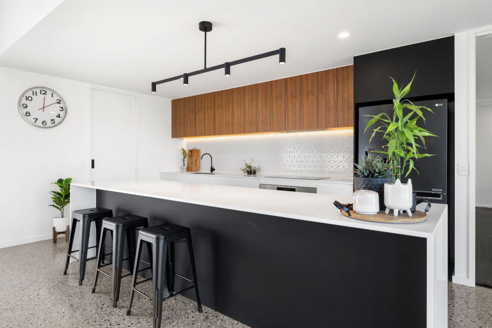 Example of a large trendy galley concrete floor and gray floor open concept kitchen design in Geelong with an undermount sink, flat-panel cabinets, quartz countertops, white backsplash, mosaic tile backsplash, black appliances, an island, white countertops and black cabinets